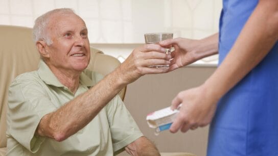 elderly man given water by caretaker