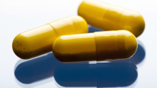 Three yellow capsules on blueish, reflective background.